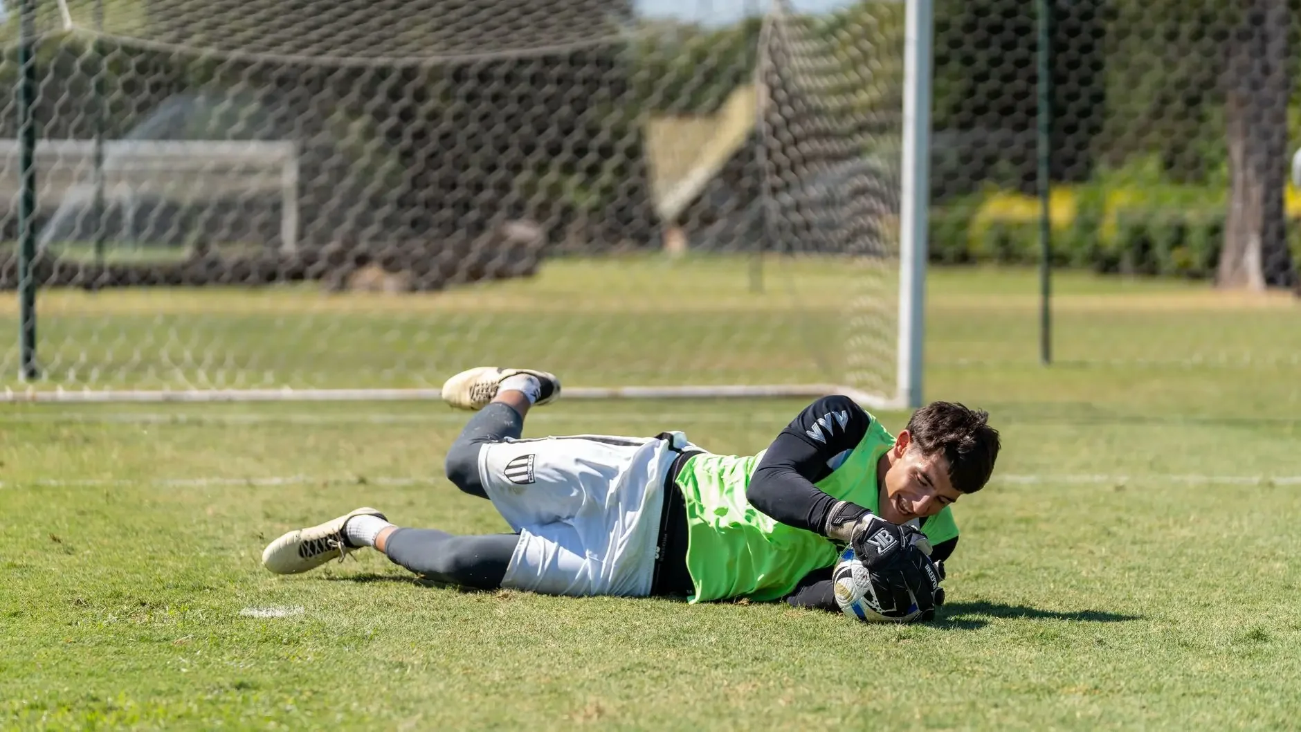 Goalkeeper Zion Suzuki diving on the grass during a training session wearing a lime green vest and white shorts.